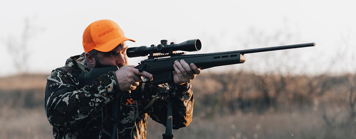 Magpul Wordmark Blaze Orange Trucker on man with camo shouldering a scoped rifle with Magpul Hunter Stock.