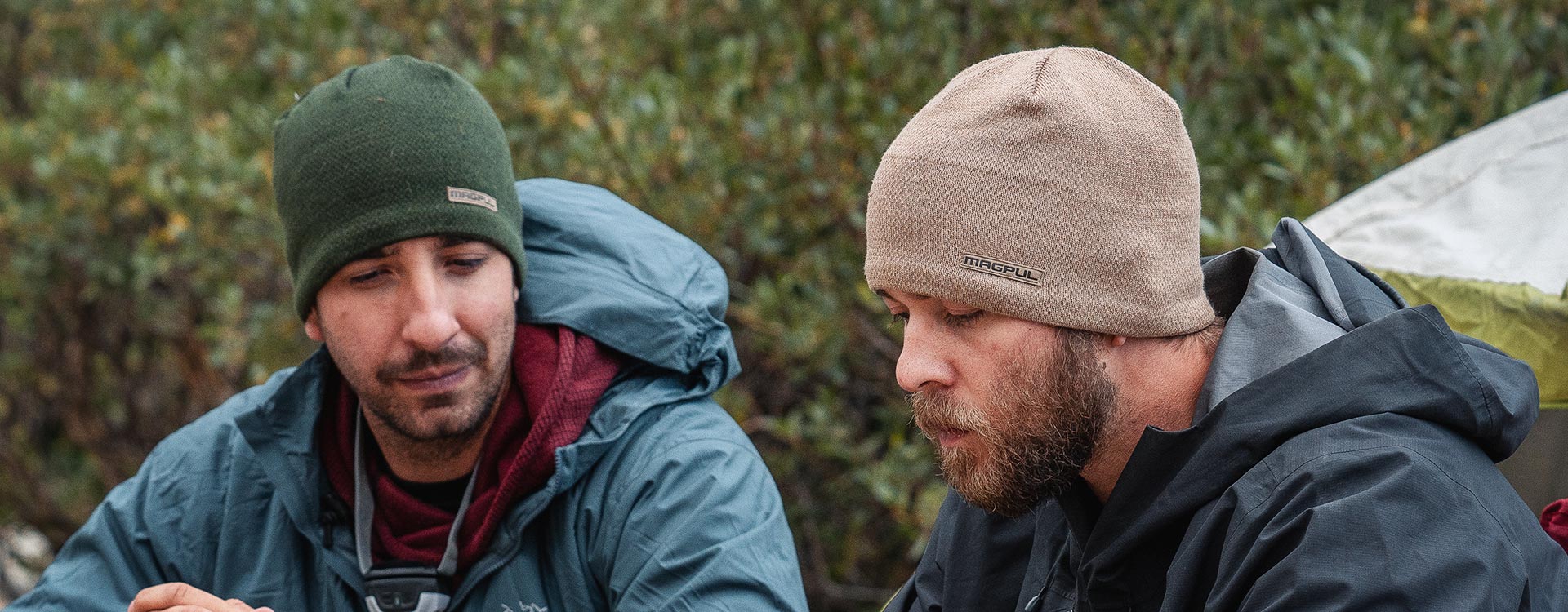 Green and Brown Magpul Tundra Beanies worn by two jacketed men camping outdoors with a tent in the background