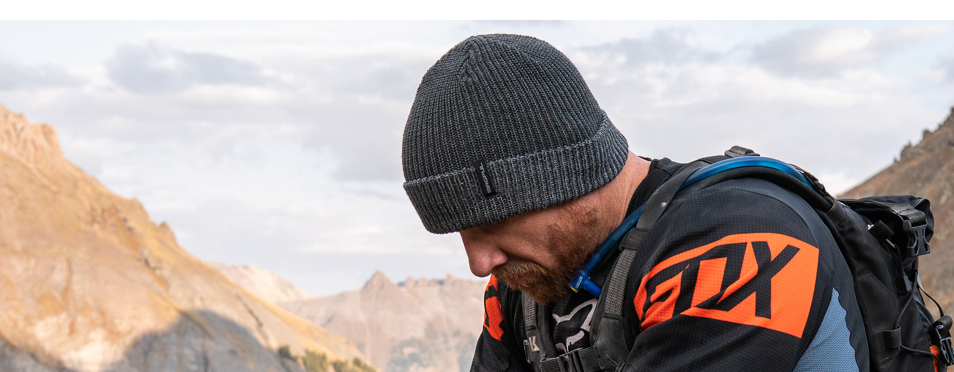 Charcoal Heather Magpul Merino Watch Cap on bearded man in technical gear taking rest at the top of a mountain